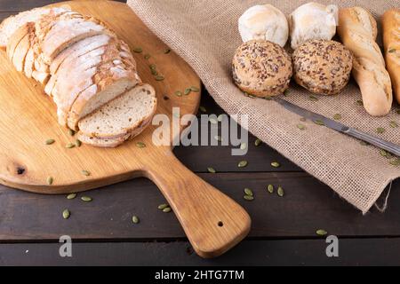 High angle view of sliced bread loaf on serving board with buns and baguettes on jute fabric Stock Photo