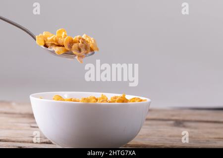 Close-up of cornflakes in spoon over breakfast bowl on table against gray background Stock Photo