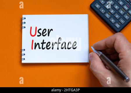 UI user interface symbol. Concept words UI user interface on white note. Businessman hand, calculator. Beautiful orange background. Copy space. Busine Stock Photo