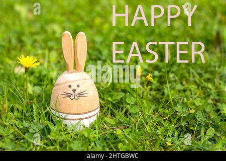 Easter Card with inscription happy Easter. Sunny green lawn with Easter decor, Wooden bunnies, greeting text. Spring time Stock Photo