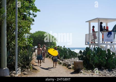 El Tunco, El Salvador - January 29, 2022: Surfers walking along the rocky beach to find perfect waves for surfing. Lifeguards standing on the chair Stock Photo