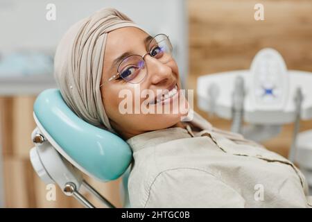 Close up portrait of young Middle-Eastern woman lying in dental chair and smiling at camera Stock Photo