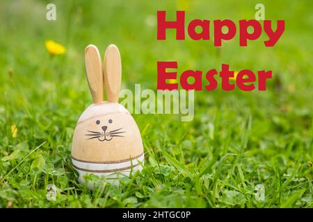 Easter Card with inscription happy Easter. Sunny green lawn with Easter decor, Wooden bunnies, greeting text. Spring time Stock Photo