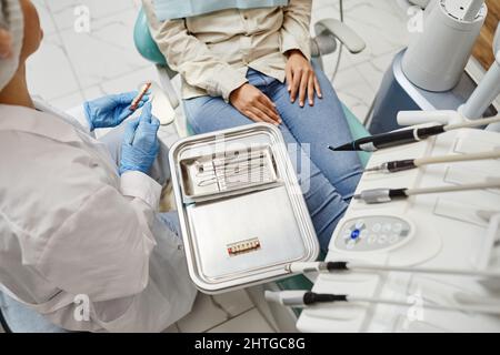 Top view of female dentist using tools on metal tray while working with patient in dental clinic, copy space Stock Photo