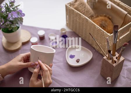 Womens hands paint a white flower ceramic pot Stock Photo