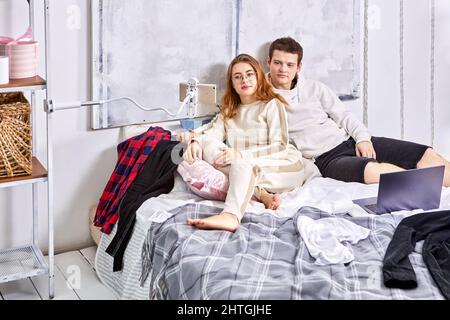 Married couple with gadgets in bed lie and watch movie on laptop. Stock Photo