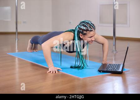 Online fitness classes using laptop for woman who stands in plank. Stock Photo