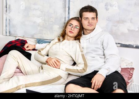 Sad young married couple lie on bed and hug during date. Stock Photo