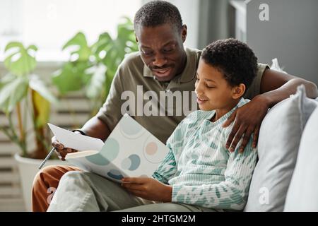 Candid portrait of happy African American father helping daughter doing homework in cozy interior Stock Photo