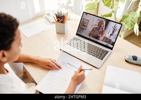 High angle view at senior teacher speaking on laptop screen during online lesson with child studying at home Stock Photo