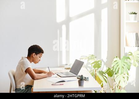 Minimal side view portrait of African American girl using laptop while studying online at home, copy space Stock Photo