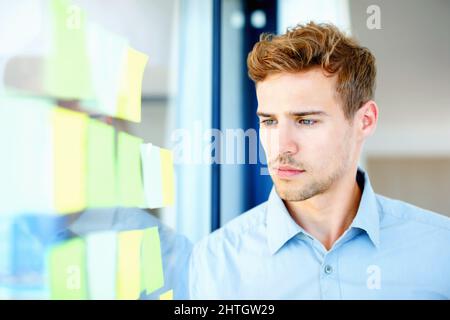 Thoughtful guy looking at adhesive notes. Thoughtful business man looking at adhesive notes on glass. Stock Photo