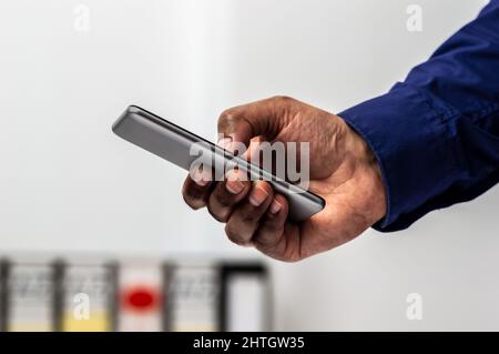 Cropped shot of an unrecognizable businessman standing alone in his home office and texting on his cellphone Stock Photo