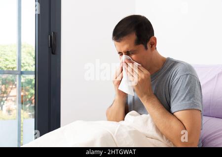 Shot of a handsome young man suffering with the flu while sitting on his bed at home Stock Photo