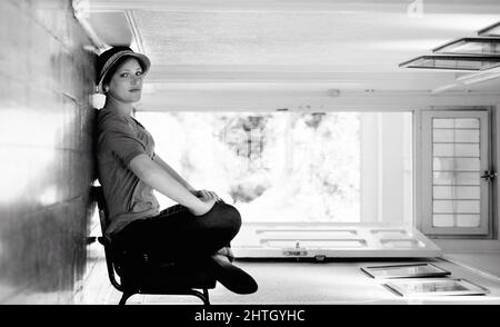 Leaning againt the floor. A woman sitting on a chair inside her house with the house turned sideways - perspective. Stock Photo