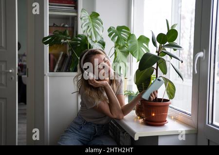 Smiling female dreaming, listening to music wear wireless headphones using mobile phone at home Stock Photo