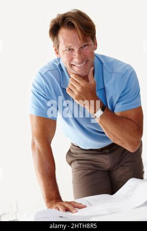 He just had a bright idea. Shot of a smiling man standing over a set of plans on a table. Stock Photo