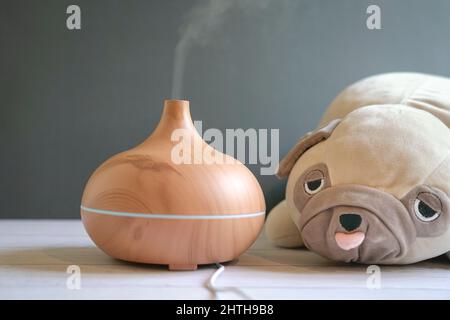 Aroma essential oil diffuser and pug dog soft toy on table. Cosy interior. Stock Photo