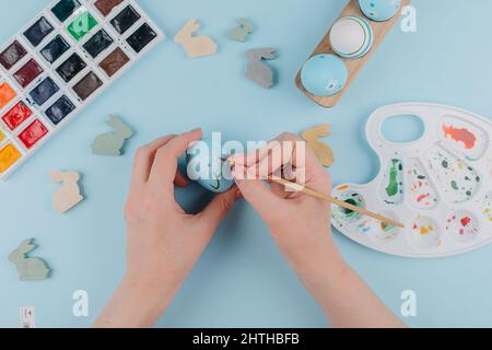 Preparation for Easter Holiday. Female hands painting Easter eggs. Flat lay, top view. Stock Photo