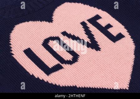 Handmade blue knitted fabric with pink heart and word Love bound on knitting needles as backgroun or texture. Stock Photo