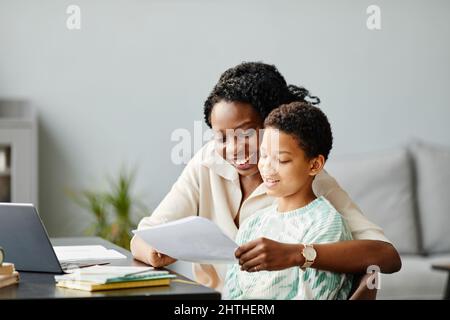 Minimal portrait of happy African American mother and daughter studying at home together and looking at test results Stock Photo