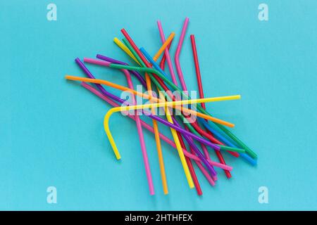 Pile of plastic disposable multi colored drinking straws for cocktails and drinks on blue background. Top view Copy space. Stock Photo