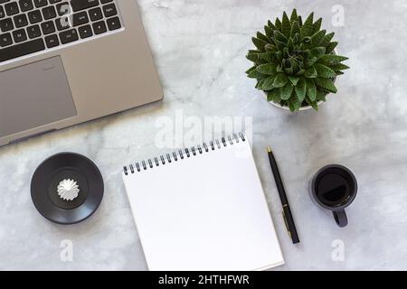 Office or home table desk. Gray laptop, open empty notepad, cup of coffee, succulent on marble background Concept stylish workplace Flat lay Top view Stock Photo