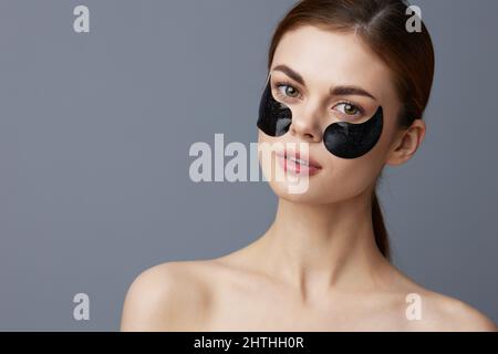 Beauty patches on the face of a woman hydrogel to moisturize the skin around the eyes. Facial skin care. Portrait on a gray background Stock Photo