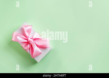 Gift box with pink silk ribbon and bow on green pastel background, top view, copy space. Celebration mother's day or birthday concept. Stock Photo