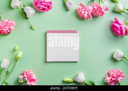 Pink, white flowers and blank notepad  frame on green pastel background, creative flat lay, copy space. Garden roses,  peonies and carnation, spring s Stock Photo