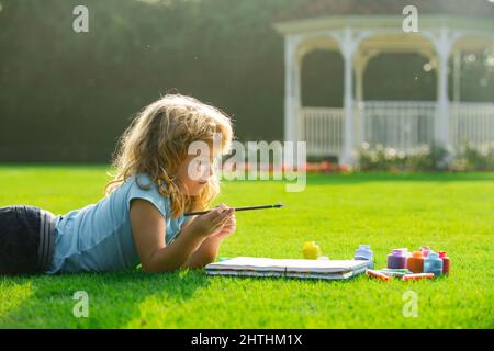 Portrait of smiling happy kid enjoying art and craft drawing in backyard or spring park. Children drawing draw with pencils outdoor. Stock Photo
