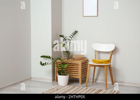 Beautiful houseplants with books on table and chair near light wall Stock Photo