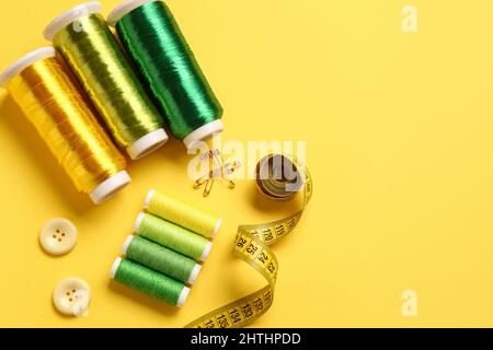 Thread spools, buttons and measuring tape on yellow background Stock Photo