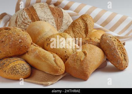 In a towel, on a wooden cutting board are different types of freshly made bread - round bread, baguette, ciabatta, buns Stock Photo