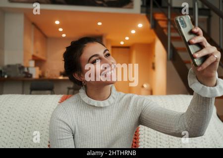 Caucasian female teen relaxing on couch taking selfies  Stock Photo