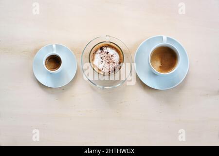 Three cups with various coffee, espresso, cappuccino and lungo crema on a light wooden table, copy space, high angle view from above, selected focus Stock Photo