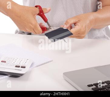 Your purchases are too extensive. Close up of a woman cutting up her credit card with a laptop and calculator in front of her. Stock Photo