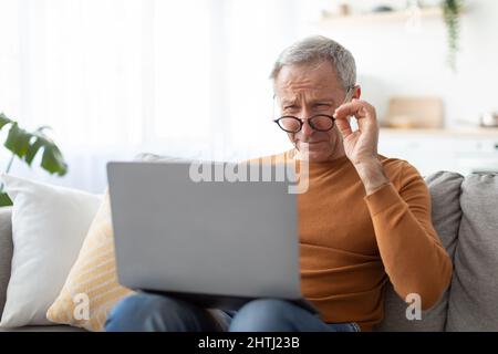 Mature man squinting using laptop, looking at screen Stock Photo