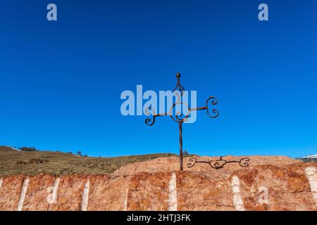 Wrought iron religious cross against a clear blue sky above an outdoor red marble altar. Lessinia Plateau Regional Natural Park. Verona, Italy Stock Photo