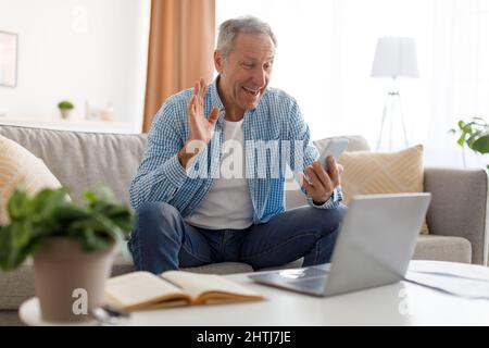 Smiling mature man waving hand using mobile phone Stock Photo