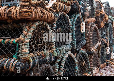 Lobster pots of green, blue, brown and fawn stand on a pebbly beach. Sharp foreground leading to soft background. Assorted colors in natural lighting Stock Photo