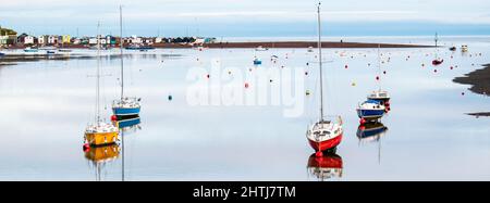 Red,Yellow and Blue boats with colorful buoys behind. Low tide cast perfect reflections on the mirror flat water. Teignmouth sits in the background. Stock Photo