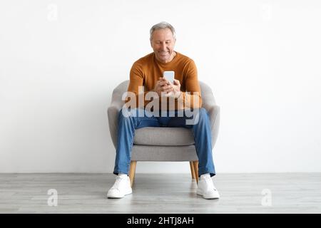 Portrait of smiling mature man using smartphone sitting on chair Stock Photo