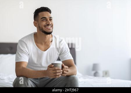 Happy Young Arab Man Relaxing On Bed With Cup Of Coffee Stock Photo