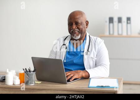 Portrait of smiling doctor looking at camera sitting at desk Stock Photo