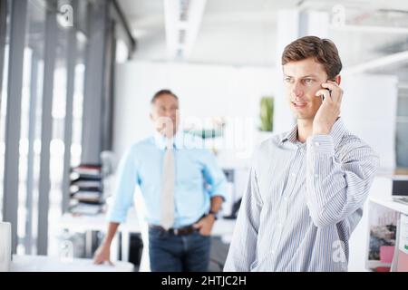 Getting updated on the design brief. A young professional talking on his cellphone as a colleague stands in the background. Stock Photo