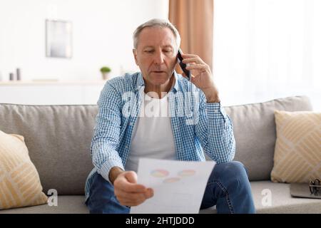 Focused mature man holding paper reading report talking on phone Stock Photo