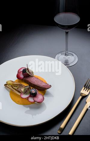 Top view of appetizing beef with sweet potato puree served with tasty artichoke on white plate on black background with cutlery and red wine Stock Photo