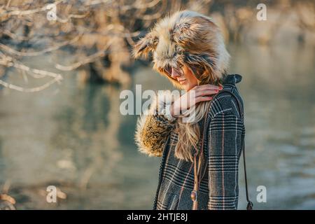 Positive adult female in stylish outfit looking away while talking on smartphone near building wall in daytime Stock Photo