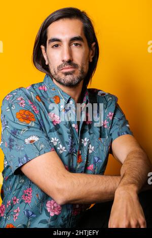 Thoughtful bearded male with dark hair standing looking at camera on yellow background in light studio Stock Photo
